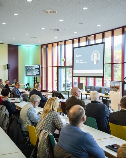 Großer Konferenzraum mit vielen sitzenden Teilnehmenden, vorne hält eine Person am Pult einen Vortrag
