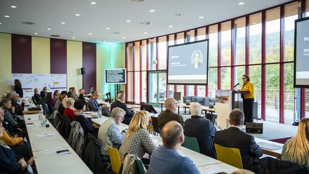 Großer Konferenzraum mit vielen sitzenden Teilnehmenden, vorne hält eine Person am Pult einen Vortrag