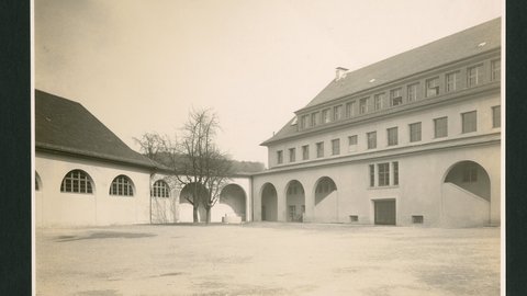 Innenhof mit Arkadengängen und zwei Gebäuden, eines mit Satteldach und das andere mit Walmdach
