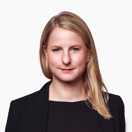 "Porträtfoto einer Frau mit schulterlangen, hellbraunen Haaren. Sie trägt einen schwarzen Blazer über einem schwarzen Shirt und blickt selbstbewusst in die Kamera. Die Hände befinden sich in den Hosentaschen. Der Hintergrund ist weiß."