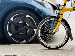 Vorderes Rad eines gelben Fahrrads vor einem geparkten Auto mit schwarzem Rad.