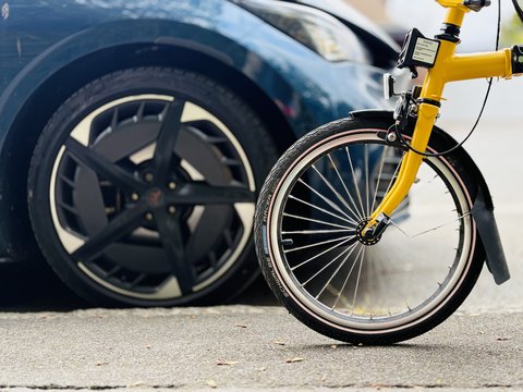 Vorderes Rad eines gelben Fahrrads vor einem geparkten Auto mit schwarzem Rad.