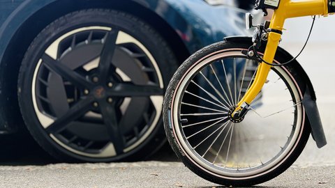 Vorderes Rad eines gelben Fahrrads vor einem geparkten Auto mit schwarzem Rad.
