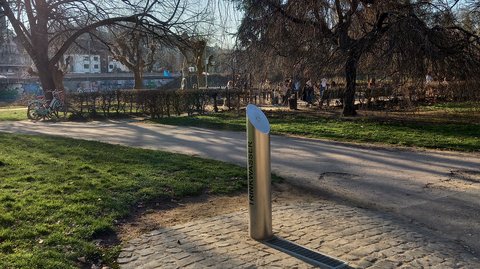 Trinkwassersäule in einem Park in Saarbrücken an einem gepflasterten Weg, umgeben von Bäumen und Grünflächen.