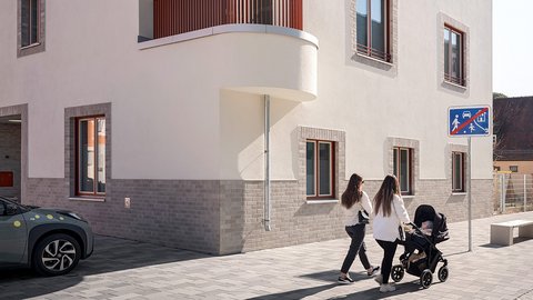 Eckgebäude mit weißer Fassade und abgerundeter Ecke, zwei Personen überqueren davor die Straße.