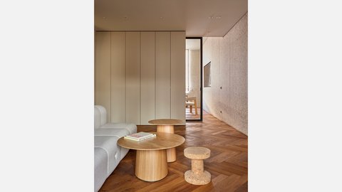 Heller Wohnbereich mit beiger Couch, runden Holztischen und Fischgrätparkett.