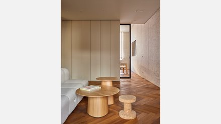 Heller Wohnbereich mit beiger Couch, runden Holztischen und Fischgrätparkett.