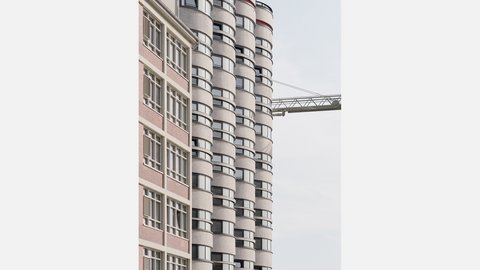 Fassaden-Nahaufnahme: links ein Backstein‑Bürohaus mit Rasterfenstern, rechts mehrere zylindrische Silotürme mit umlaufenden Fensterbändern; im Hintergrund ein Kranarm vor hellem Himmel.