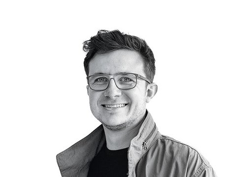 Schwarz-Weiß-Porträt eines lächelnden Philip Floegels mit Brille und Jacke vor weißem Hintergrund.