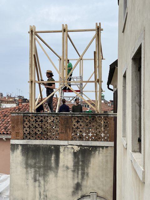 Mehrere Personen stehen auf einer Dachterrasse neben einem hohen Holzgerüst