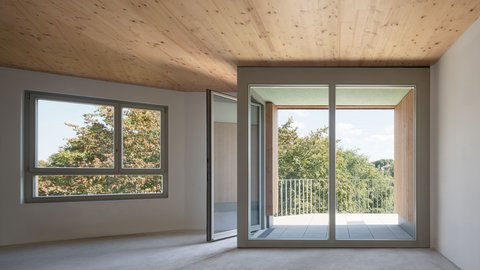 Innenraum einer modernen Wohnung mit großen Fenstern und Holzboden, mit Blick auf die grüne Umgebung.