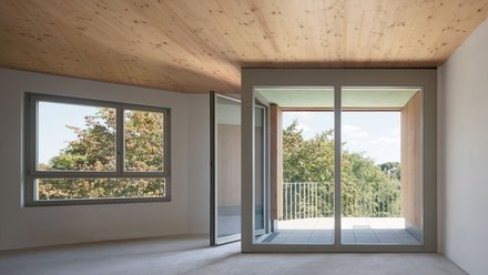Innenraum einer modernen Wohnung mit großen Fenstern und Holzboden, mit Blick auf die grüne Umgebung.