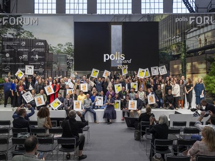 Gruppenfoto einer Preisverleihung; zahlreiche Personen halten Urkunden vor Leinwand „polis award 2025“.