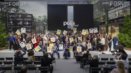 Gruppenfoto einer Preisverleihung; zahlreiche Personen halten Urkunden vor Leinwand „polis award 2025“.