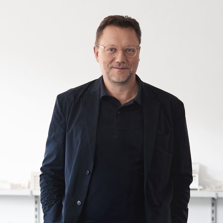 Mann mit Brille in dunkler Kleidung vor hellem Hintergrund.