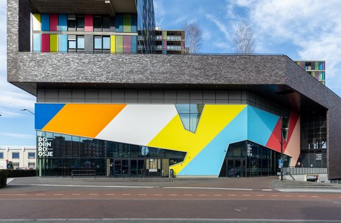 Modernes Geschäftsgebäude mit markanter, geometrisch bunt gestalteter Fassade und darüberliegenden Wohnbereichen mit farbigen Fassadenelementen