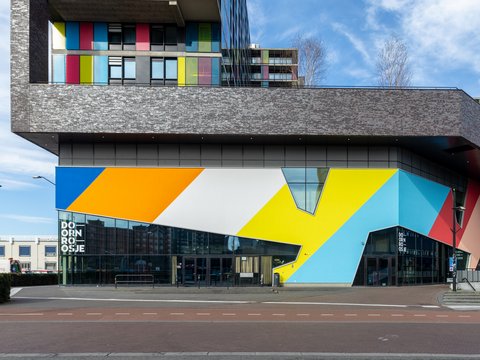 Modernes Geschäftsgebäude mit markanter, geometrisch bunt gestalteter Fassade und darüberliegenden Wohnbereichen mit farbigen Fassadenelementen