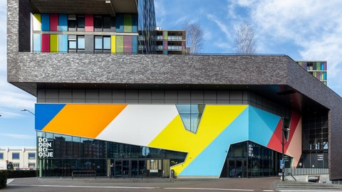 Modernes Geschäftsgebäude mit markanter, geometrisch bunt gestalteter Fassade und darüberliegenden Wohnbereichen mit farbigen Fassadenelementen