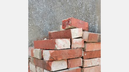 Stapel gebrauchter roter Backsteine mit Mörtelresten vor rauer Betonwand; einige Steine sind an den Kanten beschädigt.