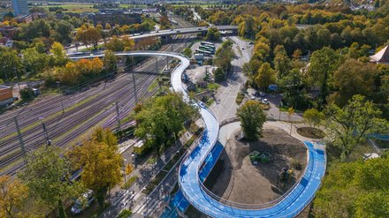 Weite Luftaufnahme der Radbrücke mit Bahnlinien, Straßen und herbstlicher Landschaft.
