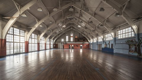 Große leere Sporthalle mit Holzboden und hohen Fenstern