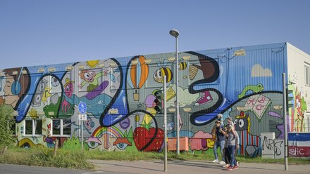 Bunt bemaltes Containergebäude mit großflächiger Street-Art und Passanten.