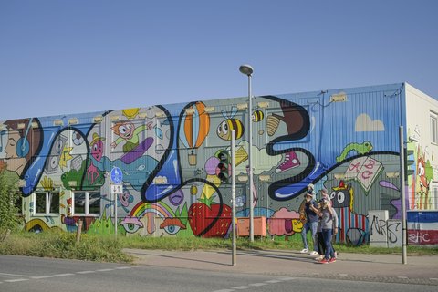 Bunt bemaltes Containergebäude mit großflächiger Street-Art und Passanten.