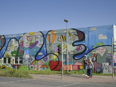 Bunt bemaltes Containergebäude mit großflächiger Street-Art und Passanten.