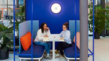 Kleiner Arbeits- und Gesprächsraum: Zwei Personen sitzen sich an einem Tisch in einer blauen Nische gegenüber.