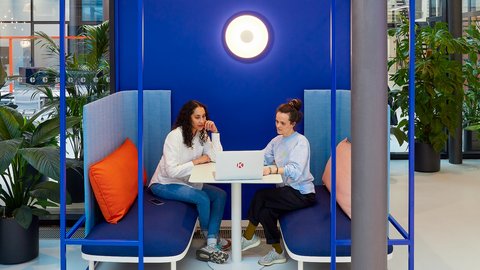 Kleiner Arbeits- und Gesprächsraum: Zwei Personen sitzen sich an einem Tisch in einer blauen Nische gegenüber.