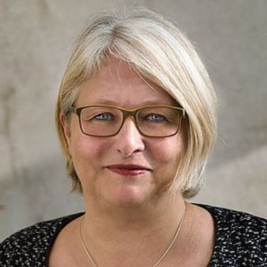 Porträt einer Frau mit Brille vor neutralem Hintergrund.