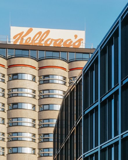 Hochhaus mit abgerundeten Balkonen und einem großen, orangefarbenen "Kellogg's"-Schriftzug auf dem Dach.