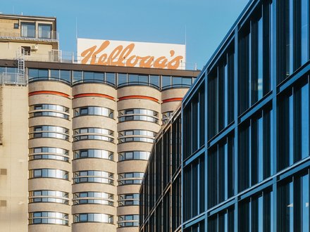 Hochhaus mit abgerundeten Balkonen und einem großen, orangefarbenen "Kellogg's"-Schriftzug auf dem Dach.