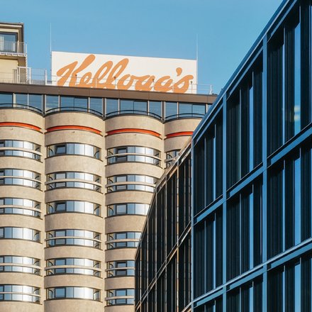 Hochhaus mit abgerundeten Balkonen und einem großen, orangefarbenen "Kellogg's"-Schriftzug auf dem Dach.