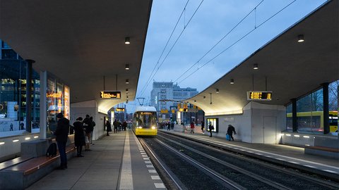Straßenbahnhaltestelle mit wartenden Fahrgästen und einfahrender Bahn bei Dämmerung.