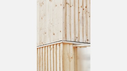 Nahaufnahme der sägerauen vertikalen Holzschalung an einer Gebäudeecke mit präzisem Metallanschluss.