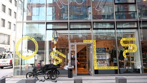 Straßenansicht eines Glasgebäudes mit geöffnetem Eingang und Ausstellung im Erdgeschoss.