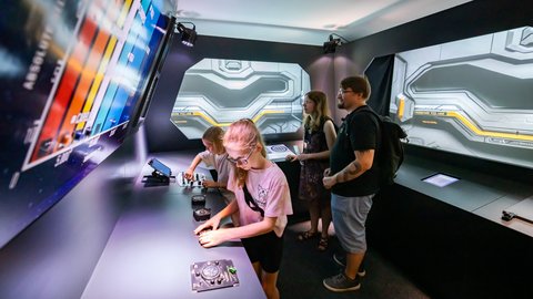 Mehrere Personen interagieren mit digitalen Touchscreens in einem modernen Ausstellungsraum mit futuristischen Wandprojektionen