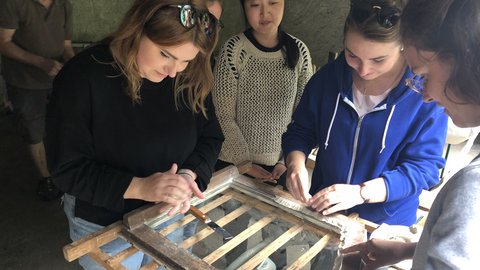 Mehrere junge Frauen betrachten und berühren einen alten Holzrahmen mit Gitterstäben in einem Innenraum