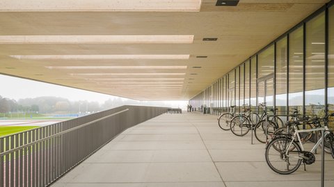 Überdachter Laubengang mit Fahrradstellplätzen entlang der Glasfassade.