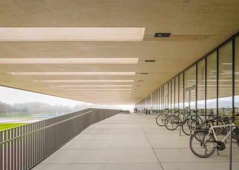 Überdachter Laubengang mit Fahrradstellplätzen entlang der Glasfassade.