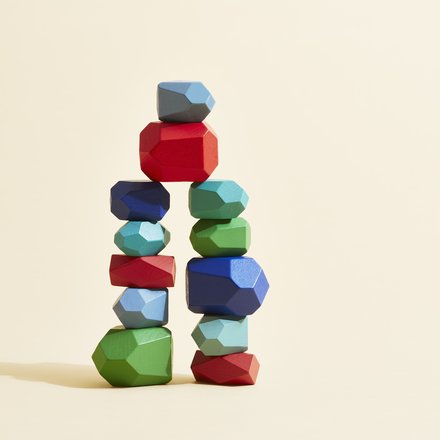 Mehrfarbige, geometrische Holzsteine sind zu einer stehenden Figur gestapelt.