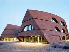 Moderne Schulgebäude mit geneigten Fassaden aus dunklen Holzschindeln auf offenem Platz.