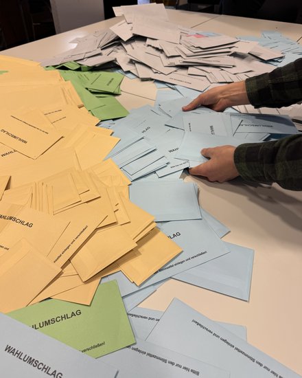 Zwei Hände die nach blauen, grünen und gelben Wahlscheinen greifen