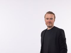Mann in schwarzem Sakko und schwarzem T-Shirt und rötlichen nach hinten gebürsteten Haaren