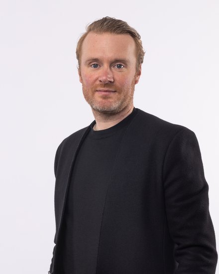 Mann in schwarzem Sakko und schwarzem T-Shirt und rötlichen nach hinten gebürsteten Haaren