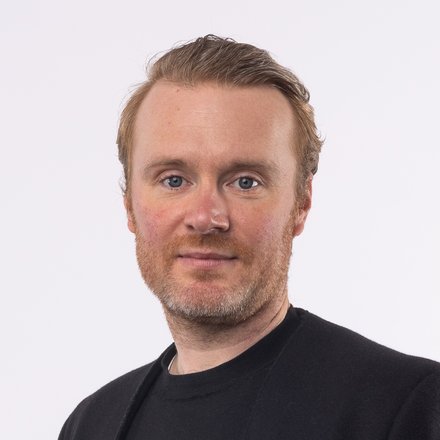 Mann in schwarzem Sakko und schwarzem T-Shirt und rötlichen nach hinten gebürsteten Haaren