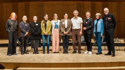 Gruppenfoto von Teilnehmenden auf einer Bühne in einem Holzsaal, vermutlich Podium oder Organisationsteam.