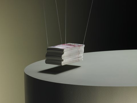 Ein Stapel Printmagazine, an dünnen Fäden aufgehängt, schwebt knapp über einem runden Podest; dunkler Studiohintergrund und weiches Seitenlicht.