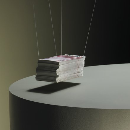 Ein Stapel Printmagazine, an dünnen Fäden aufgehängt, schwebt knapp über einem runden Podest; dunkler Studiohintergrund und weiches Seitenlicht.